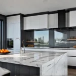 A sunlit modern kitchen with sleek white cabinetry stainless steel appliances andfeat
