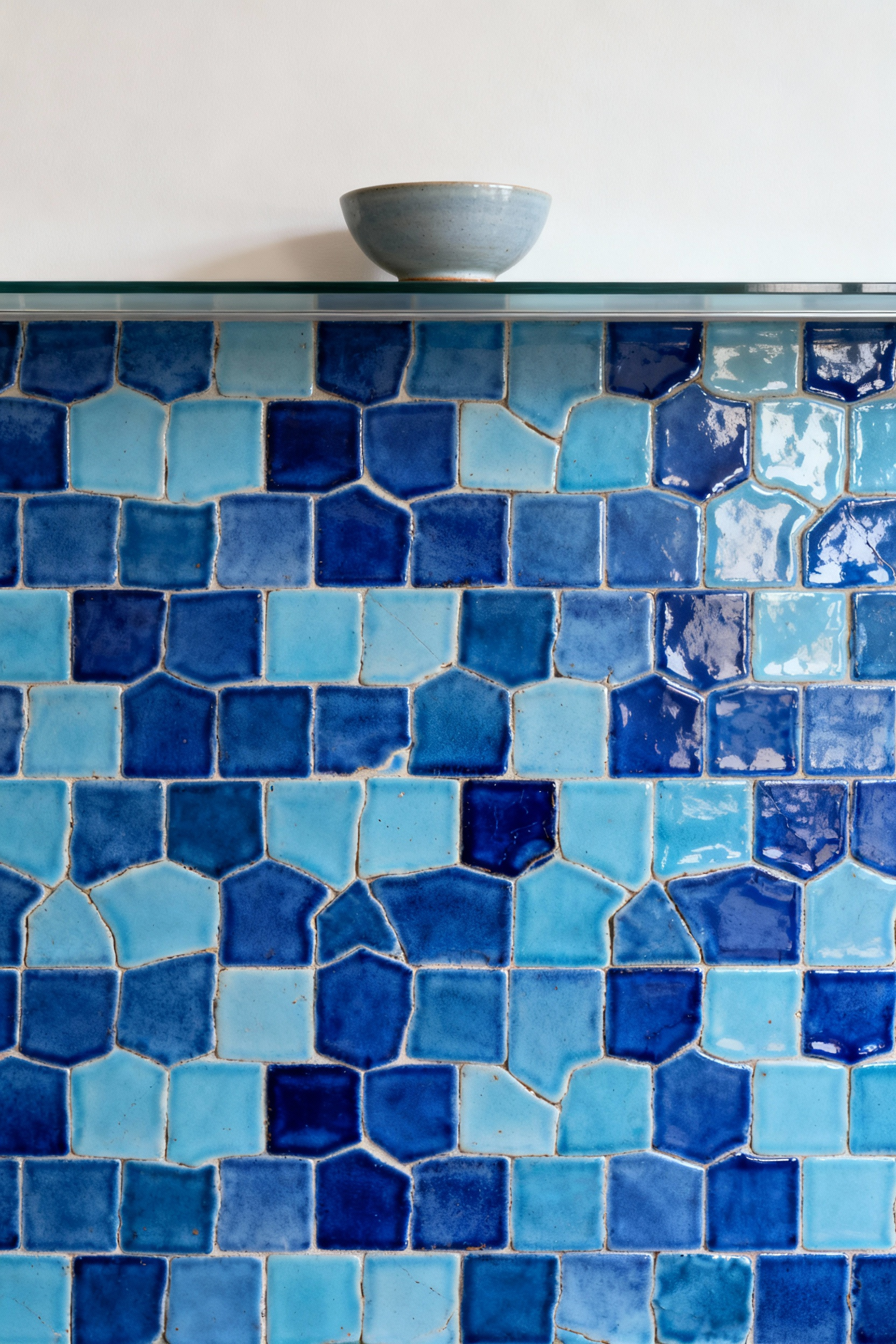 Close-up of a blue kitchen backsplash featuring hand-cut Zellige tiles in various shades of blue, showcasing textural depth and unique glaze variations under soft ambient light.