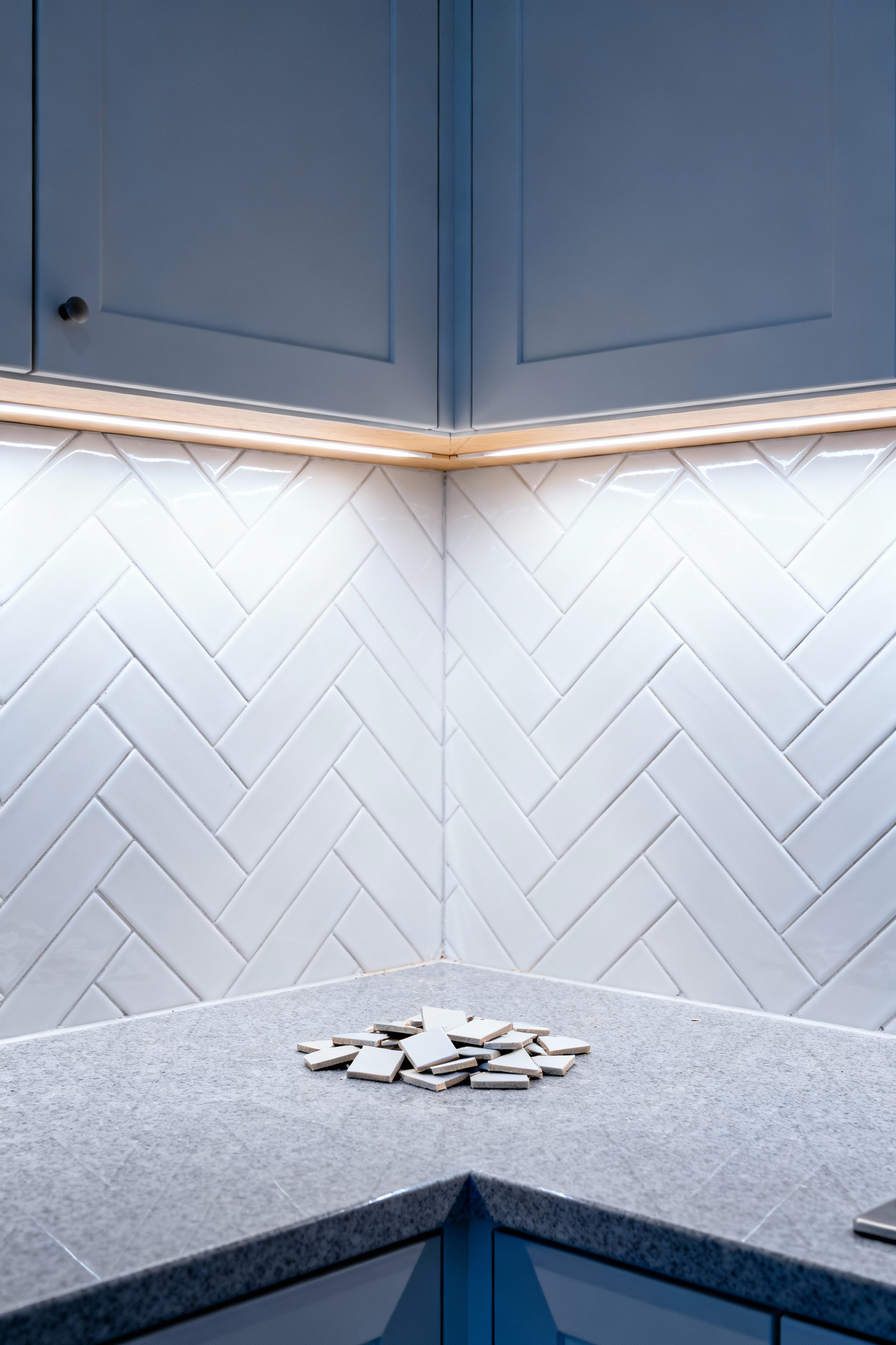 A modern kitchen installation featuring a detailed white ceramic herringbone tile backsplash wrapping tightly around an internal corner, illustrating the complexity and high material waste percentage required for intricate geometric patterns.