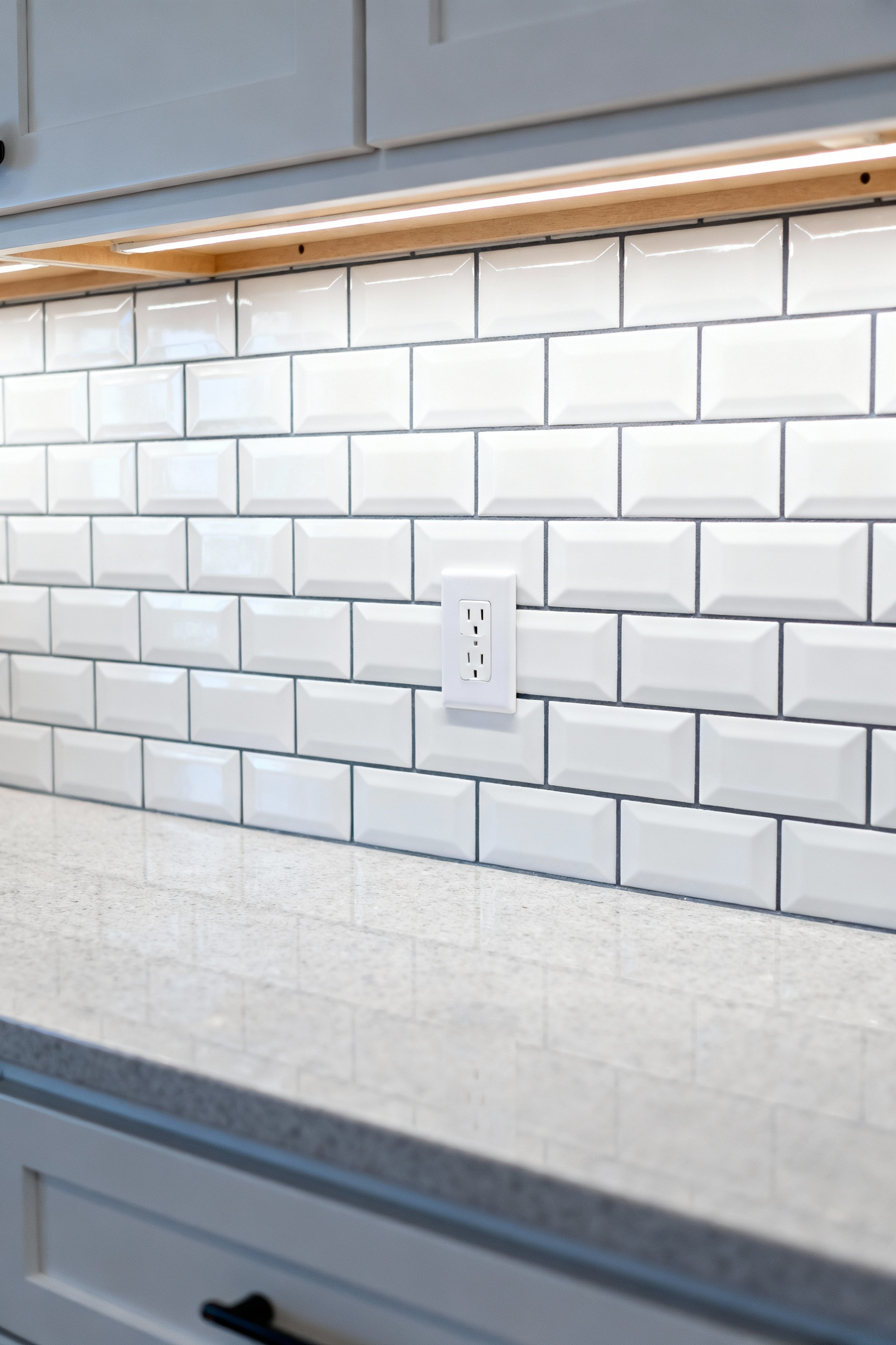 Detailed image showing a modern kitchen backsplash made of white subway tile with dark grout, featuring a horizontally installed electrical outlet cover that aligns perfectly with the tile rows to maintain visual rhythm.