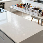 A brightly lit, clean kitchen countertop after everything has been removed, with groups of categorized kitchen items (spices, utensils, small appliances) neatly sorted in bins on an adjacent surface for a comprehensive decluttering purge.