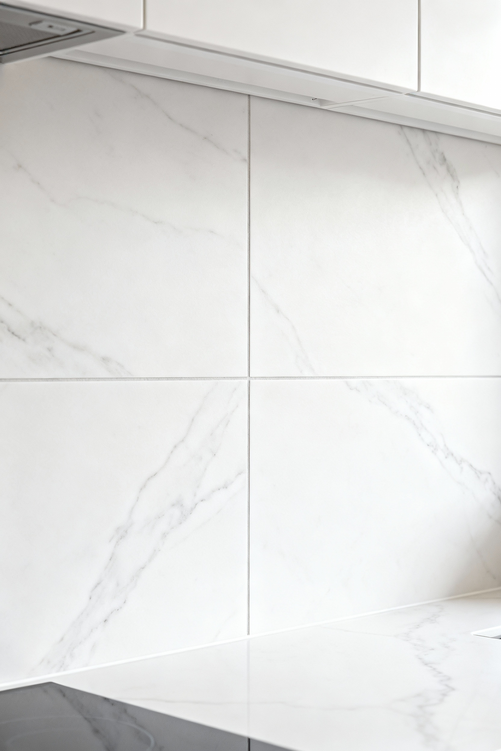 Modern kitchen backsplash featuring large-format white marble tiles with thin, color-matched white grout, creating a continuous and seamless surface that enhances spatial perception.