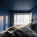 A high-end bedroom interior featuring a deep midnight blue and charcoal paint scheme designed for emotional relaxation and neuro-aesthetic appeal.