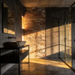 A luxury industrial bathroom featuring textured concrete walls and exposed brick highlighted by warm side lighting to create a sense of depth and warmth.